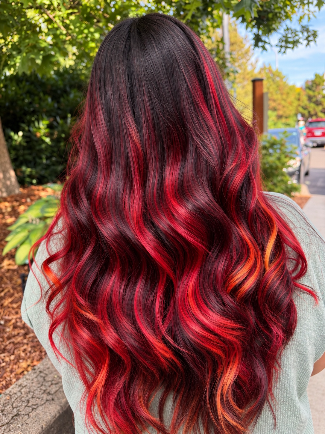 Vivid custom flame hair color melting from dark roots into red, copper and golden-yellow waves